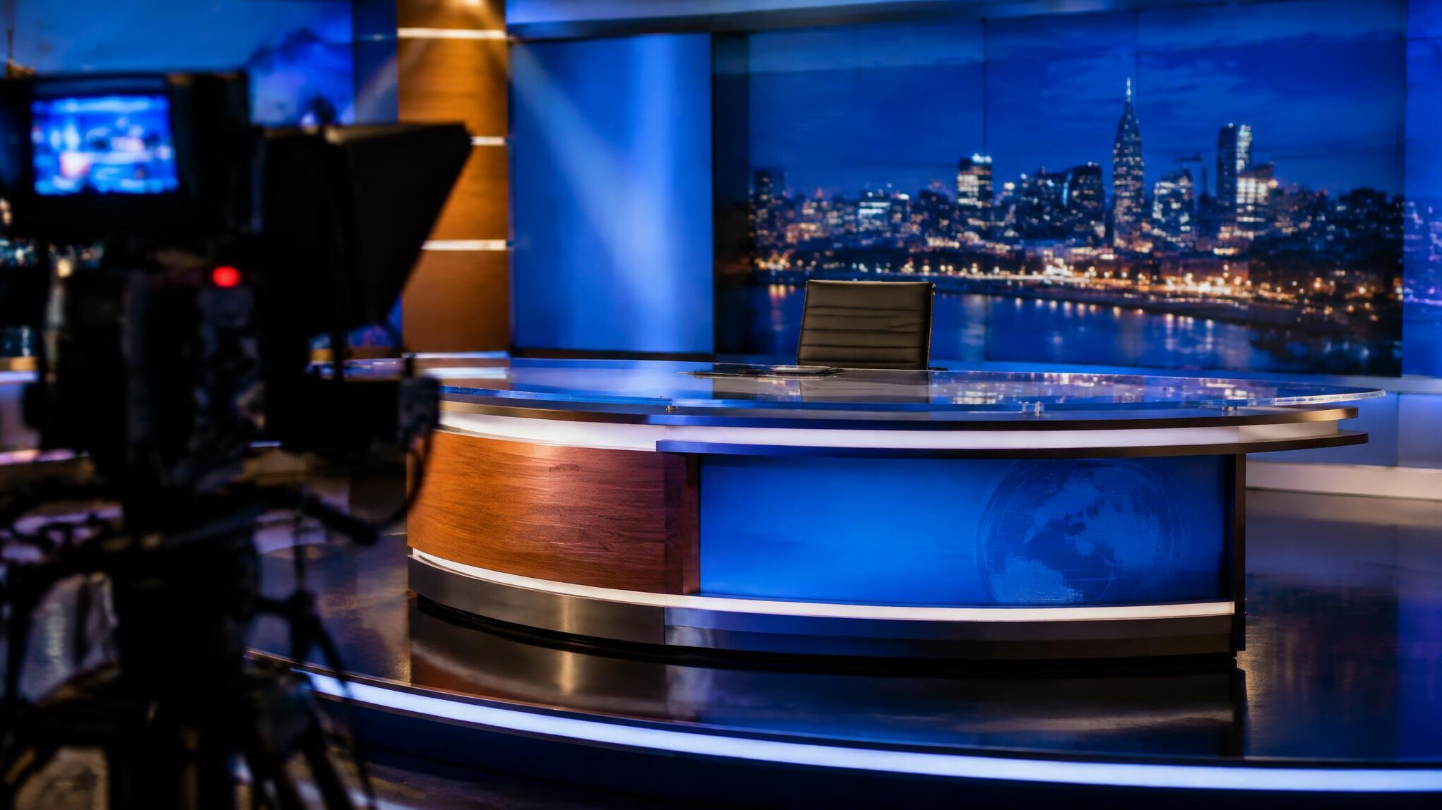 Empty television news presenter desk lit by studio lights